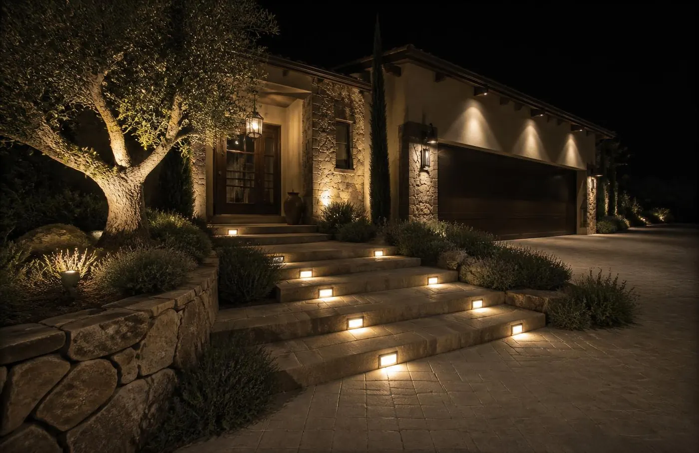 Same entry after installation with lit stone treads and an uplit olive tree