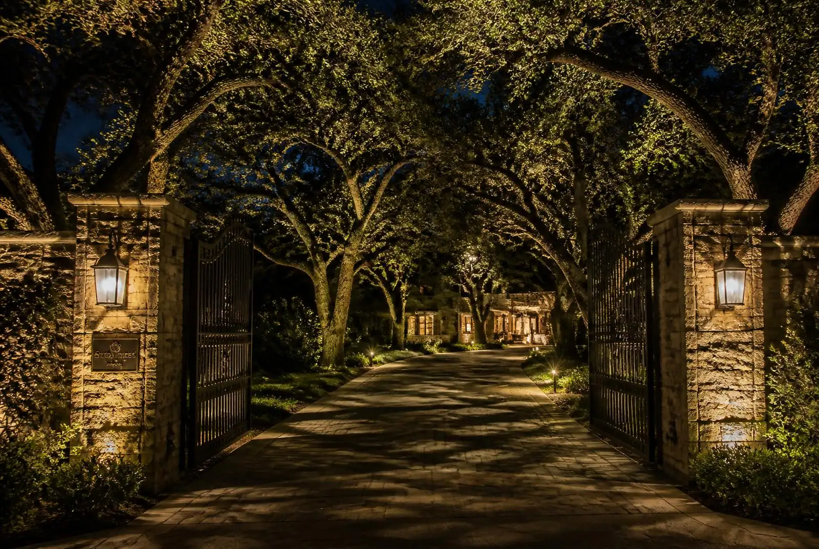 Anaheim Hills gated estate driveway with lit oaks and stone pilasters at night